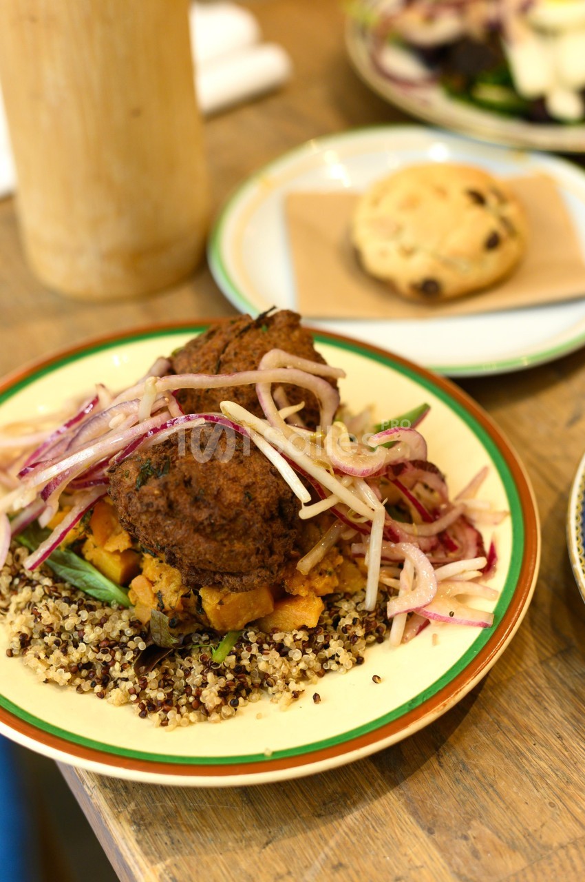 Assiette de quinoa garnie de falafels, légumes rôtis et salade d'oignons rouges, avec un cookie en arrière-plan.