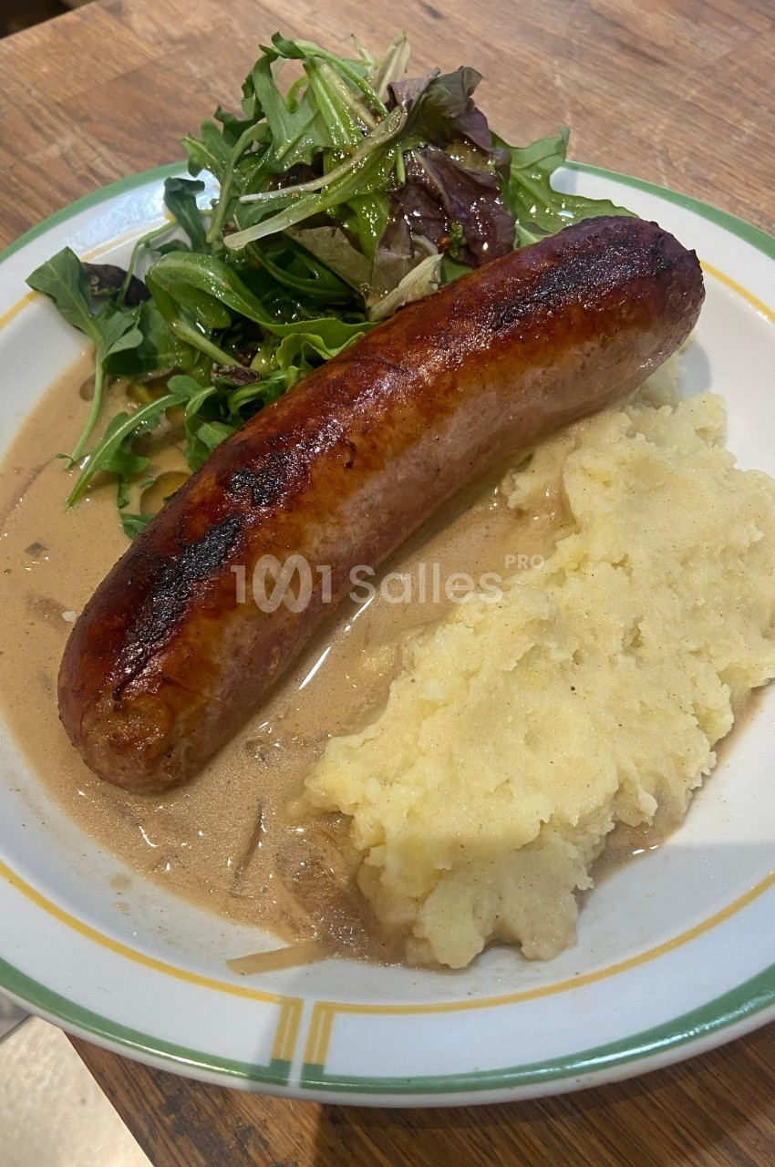 Assiette contenant une saucisse grillée, une purée de pommes de terre, une sauce brune et une salade verte.