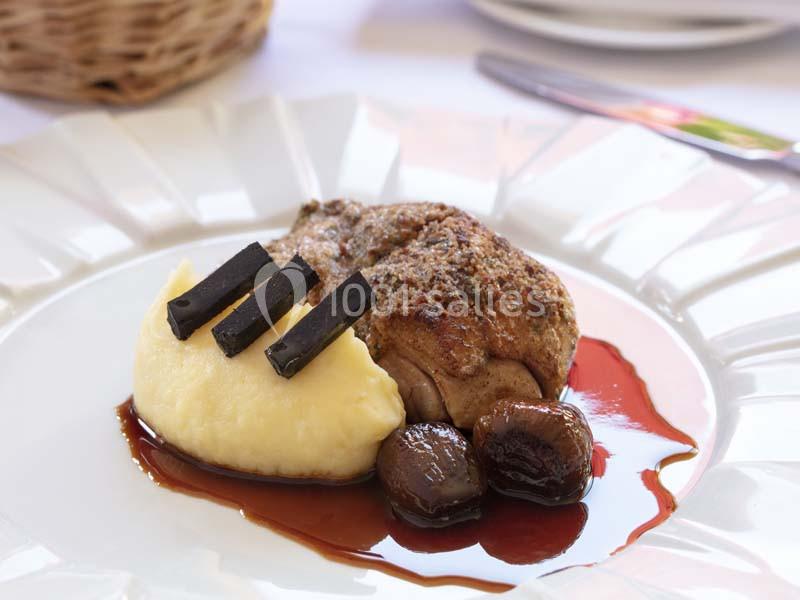 Assiette de viande accompagnée de purée, morceaux de truffe, marrons et sauce, servie sur une table dressée.