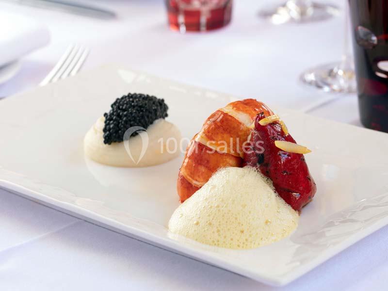 Assiette gastronomique avec homard, purée, caviar et écume, présentée sur une table dressée.