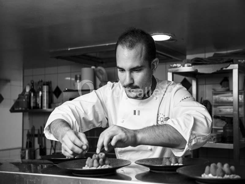 Un chef en cuisine dresse soigneusement des assiettes avec des framboises dans un environnement professionnel.