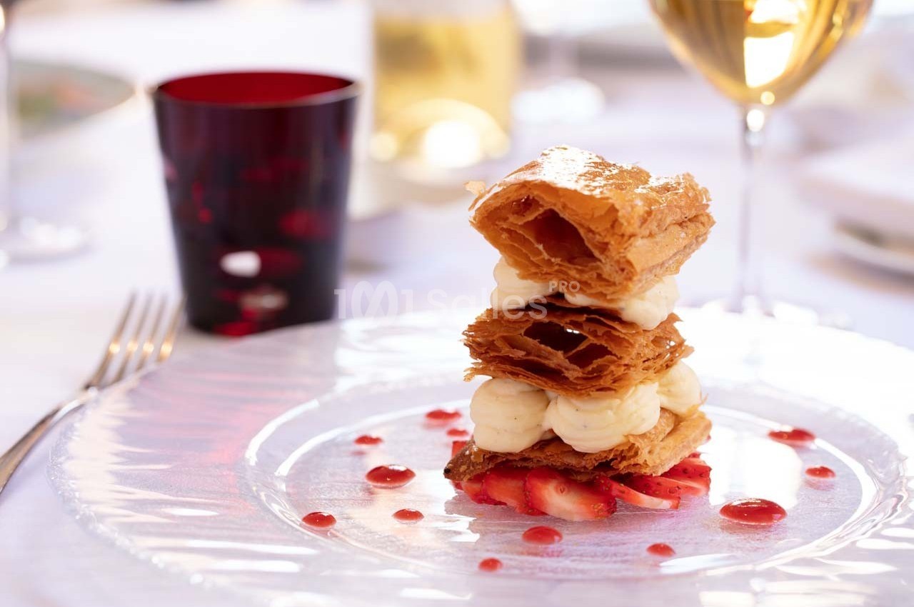 Dessert composé de couches de pâte feuilletée, crème et fraises, présenté sur une assiette avec une décoration raffinée.