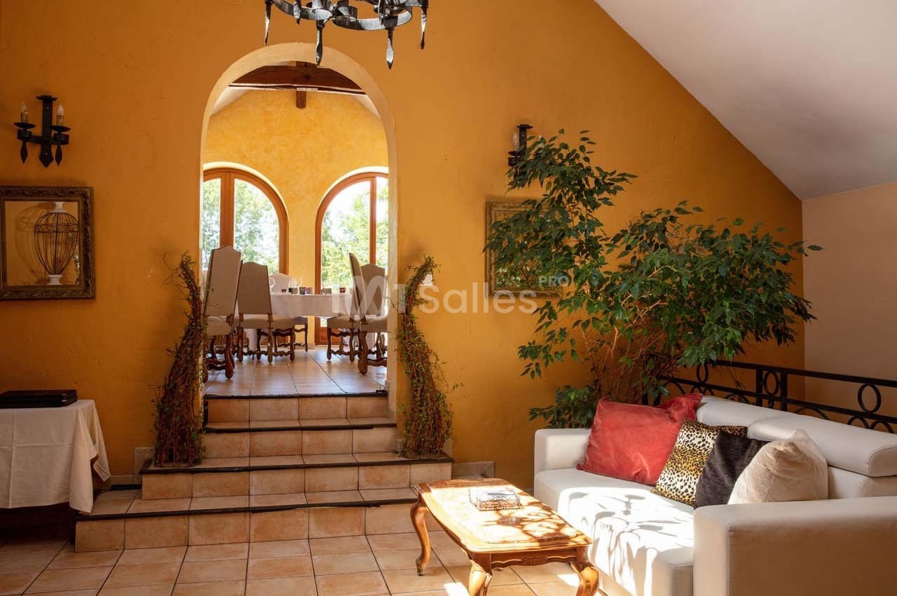 Salon lumineux avec canapé blanc, table basse en bois et plantes, menant à une salle à manger éclairée par des fenêtres…