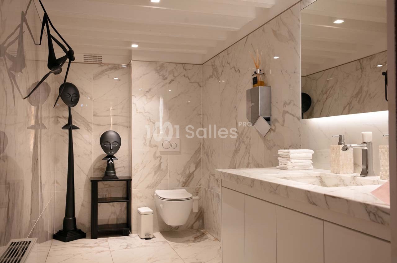 Salle de bain moderne avec murs en marbre, toilettes suspendues, lavabo avec serviettes pliées et décoration minimaliste.