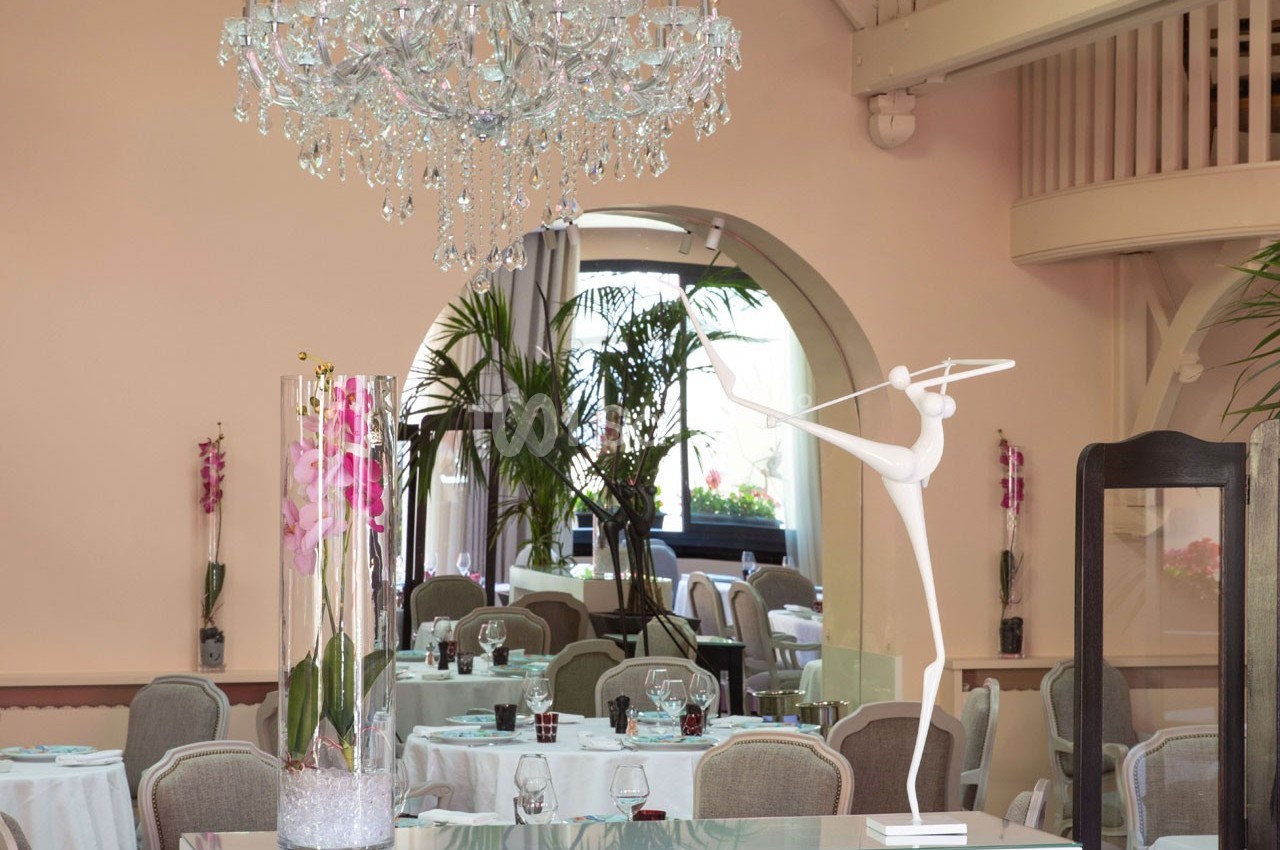 Salle de réception élégante avec tables dressées, lustre en cristal, décoration florale et sculpture moderne blanche.