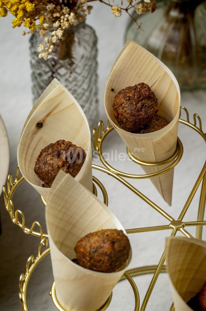 Boulettes dorées servies dans des cônes en bois, présentées sur un support doré avec des fleurs en arrière-plan.