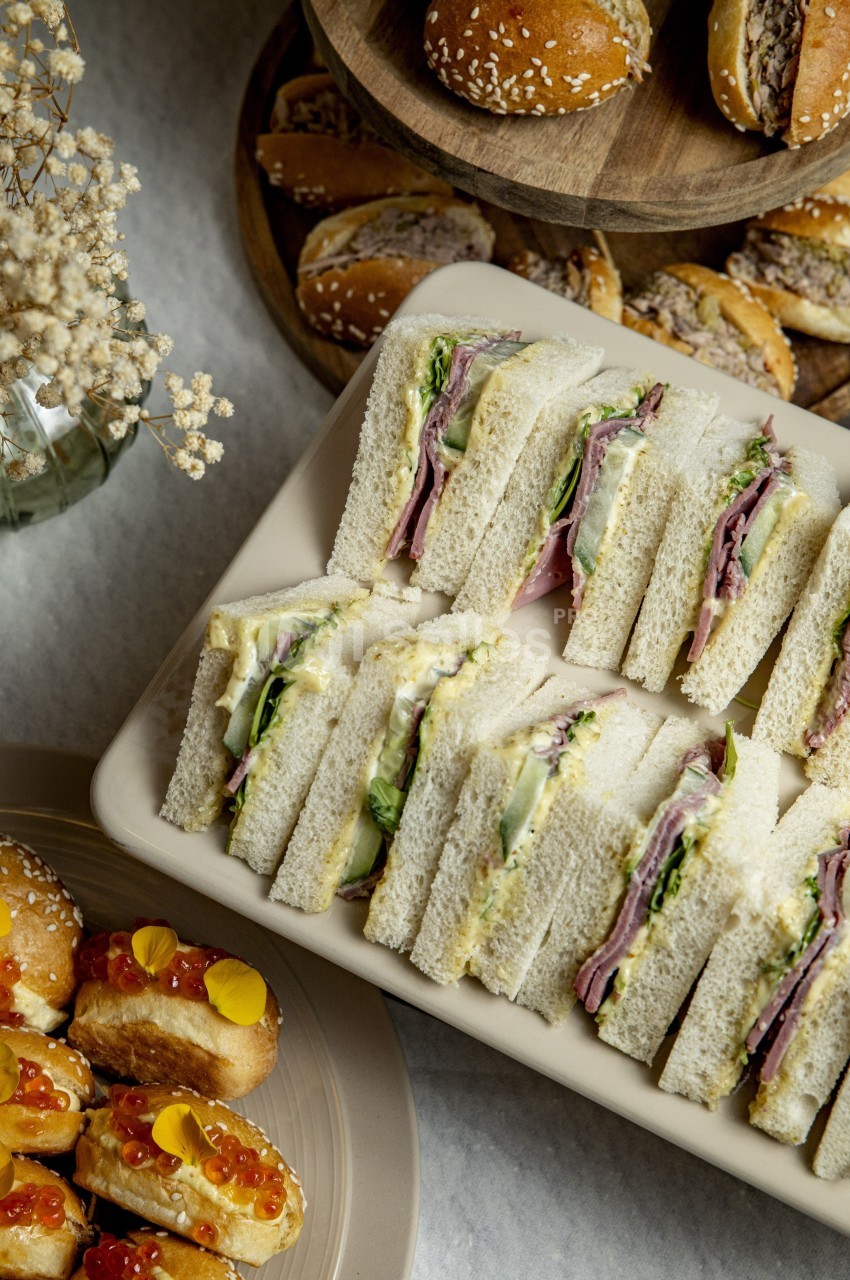 Plateau de sandwichs garnis de légumes et charcuterie, accompagné de petits pains et amuse-bouches sur une table.