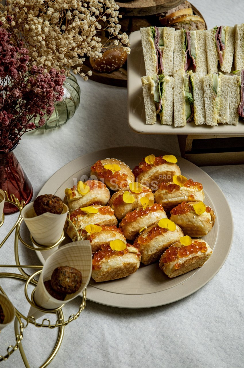 Assortiment de sandwichs, bouchées garnies d'œufs de poisson et fleurs comestibles, et snacks sur une table décorée.