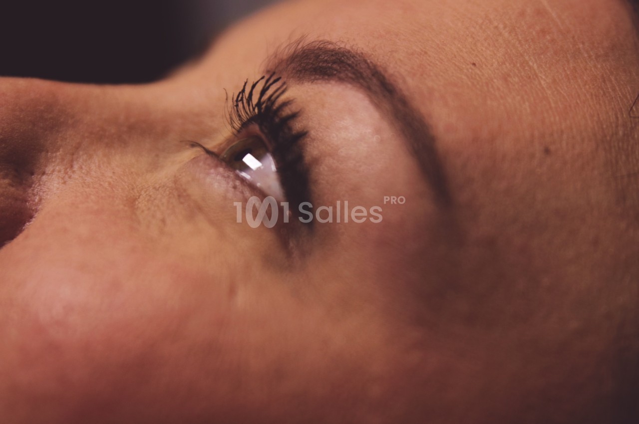 Gros plan sur le visage d'une femme, mettant en valeur son œil ouvert et ses cils sous un éclairage doux.