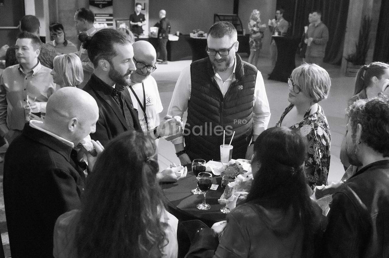 Un groupe de personnes discute autour d'une table haute lors d'un événement convivial en intérieur.