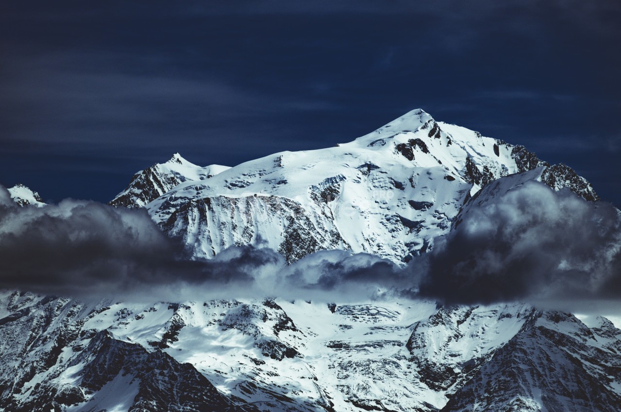 Montagne enneigée sous un ciel sombre, partiellement enveloppée de nuages bas.