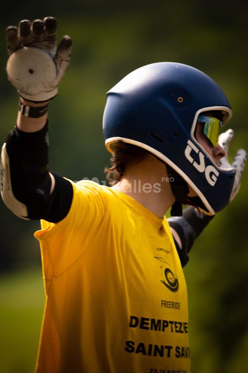Personne portant un casque et des gants, les bras levés, vêtue d'un t-shirt jaune, en extérieur verdoyant.