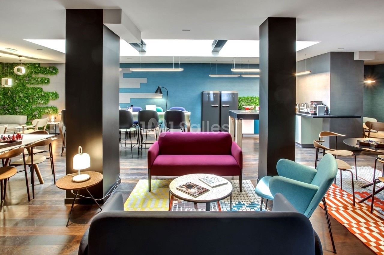 Espace intérieur moderne avec mobilier coloré, coin détente, tables, chaises et mur végétal en arrière-plan.