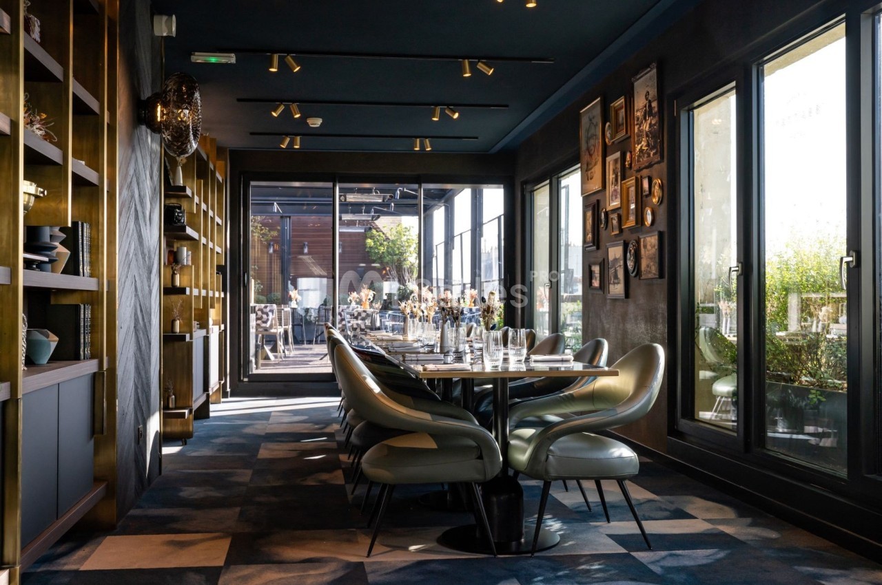 Salle de restaurant moderne avec table dressée, chaises design, étagères décoratives et grandes baies vitrées donnant sur…
