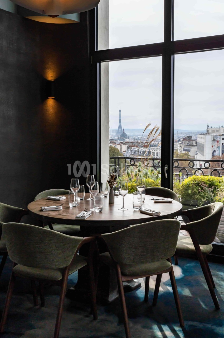 Table ronde dressée dans un restaurant avec vue sur Paris et la tour Eiffel à travers une grande baie vitrée.