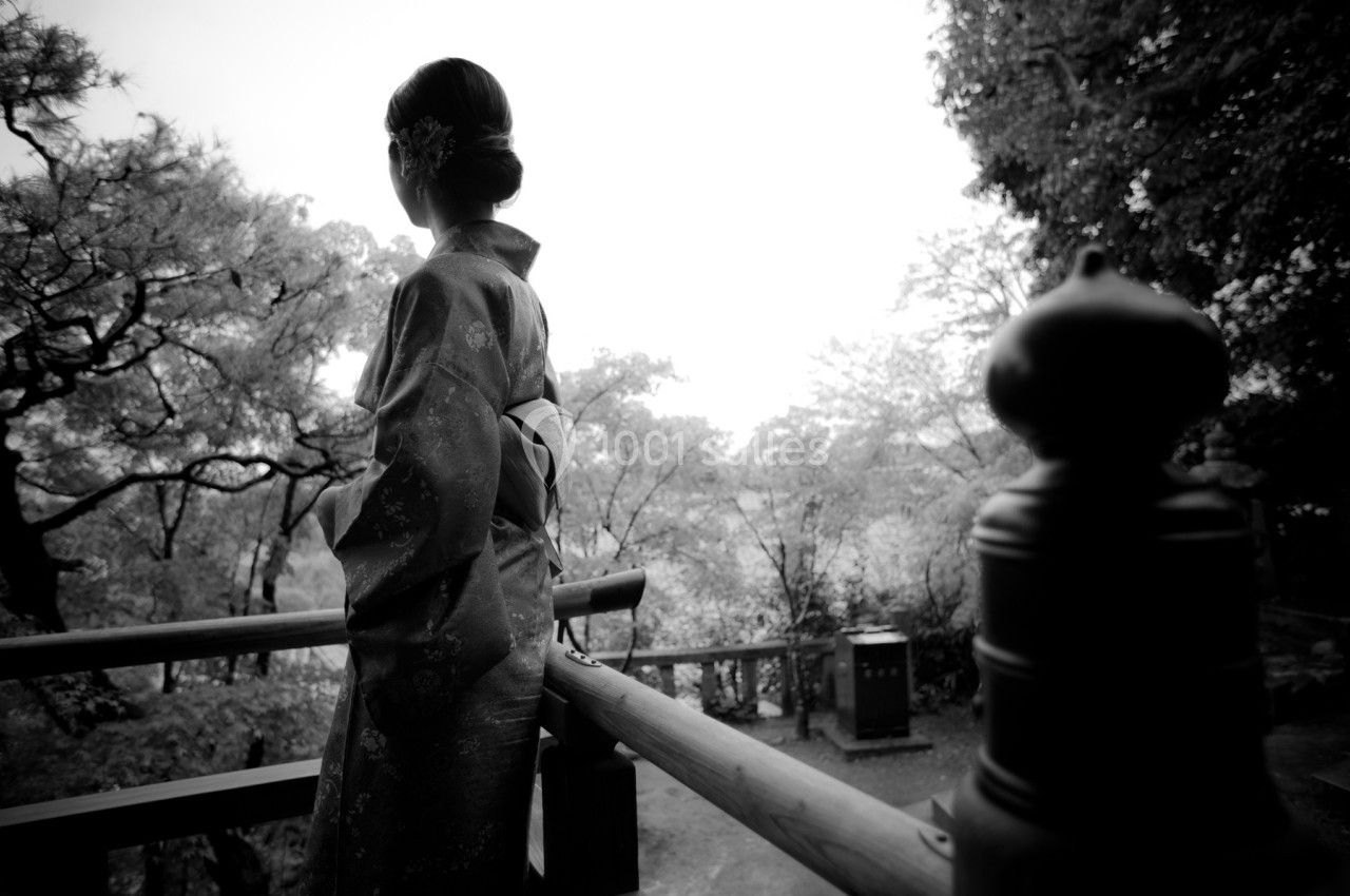 Femme en kimono vue de dos, debout sur une terrasse en bois, entourée d'arbres dans un cadre naturel.