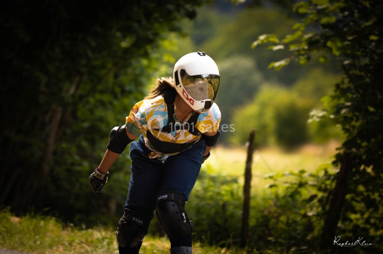 Personne en casque et protections pratiquant le longboard sur une route bordée de verdure.