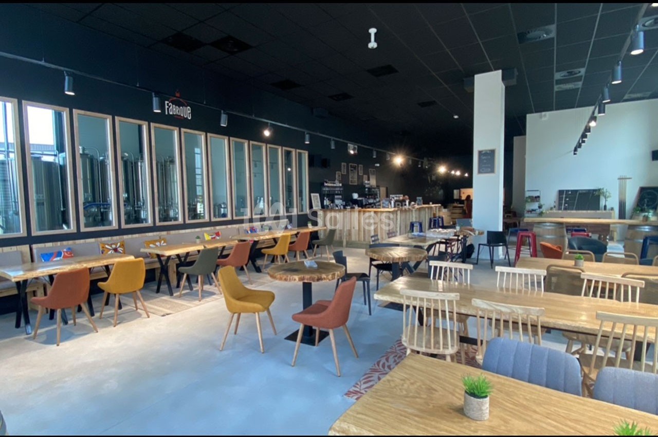 Salle de restaurant moderne avec tables en bois, chaises colorées et vue sur une zone de brassage vitrée à l'arrière.