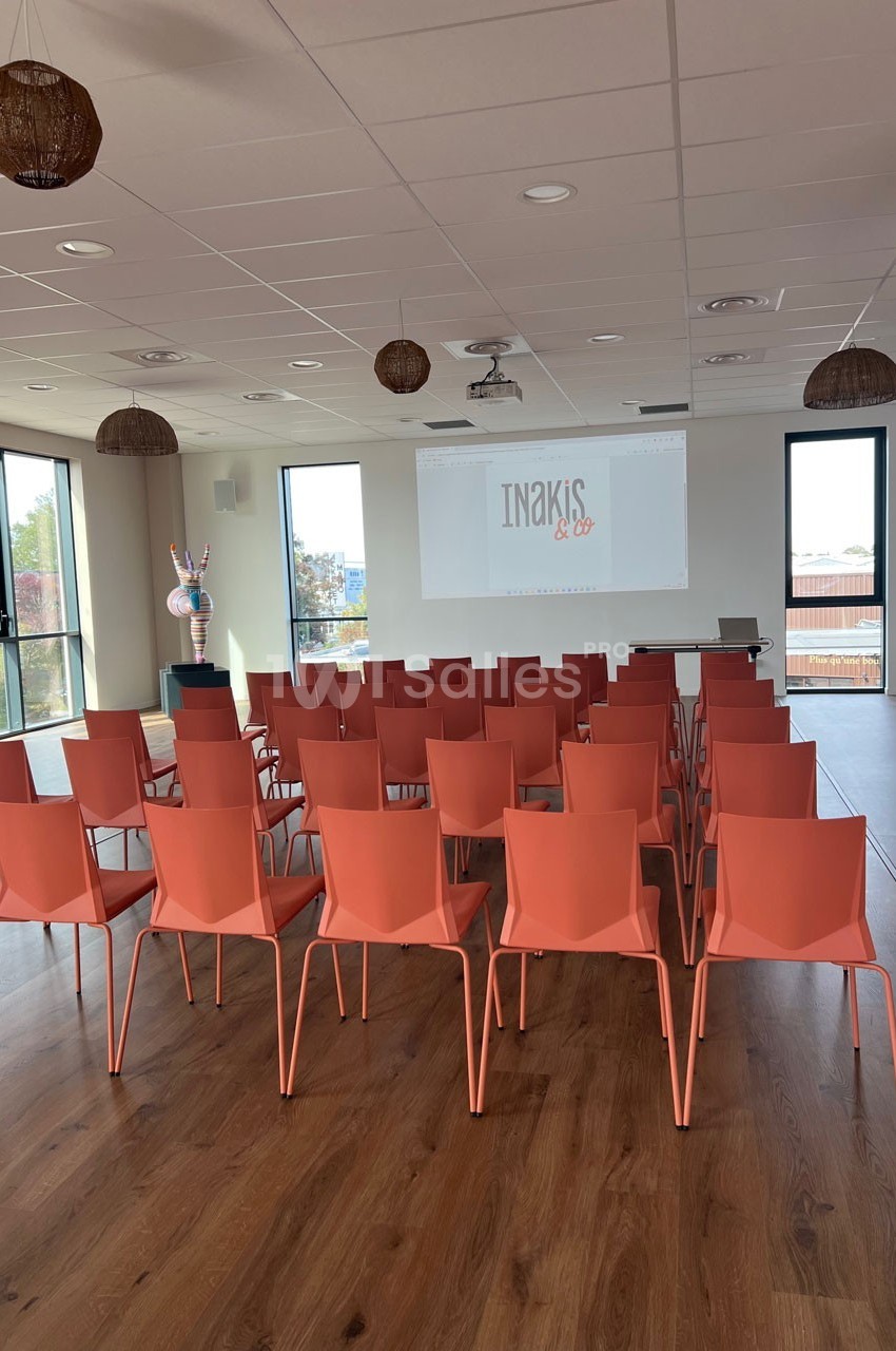 Salle de réunion lumineuse avec des chaises orange alignées face à un écran de projection.