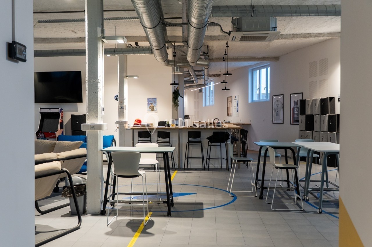 Espace de coworking moderne avec tables, chaises, canapé et décoration industrielle.