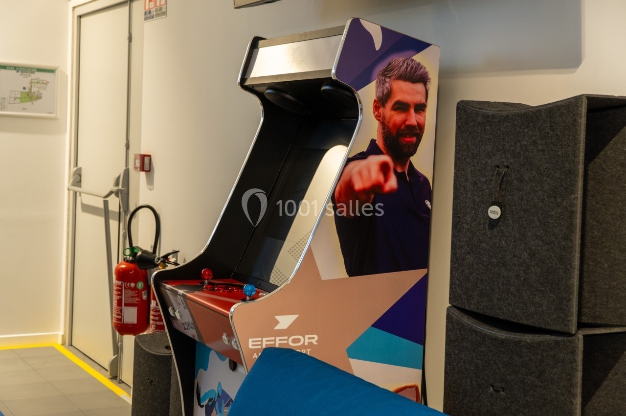 Borne d'arcade rétro avec un visuel d'homme pointant du doigt, placée dans un espace intérieur moderne.