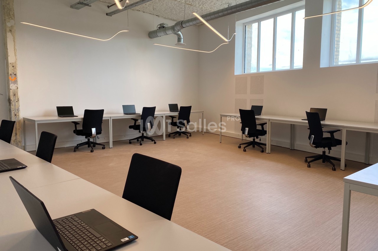 Salle de travail lumineuse avec plusieurs bureaux équipés de chaises et d'ordinateurs portables.