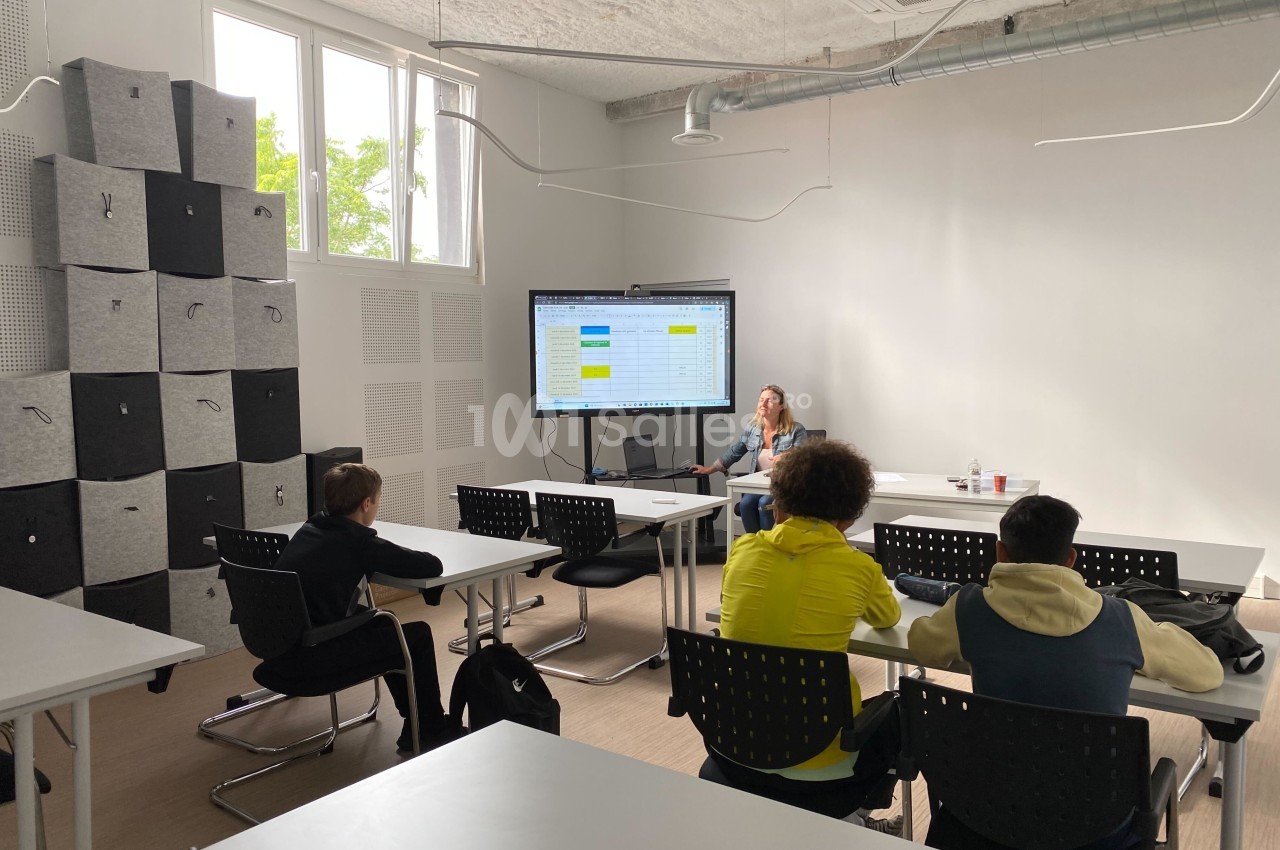 Une formatrice présente un tableau sur un écran à un petit groupe de personnes dans une salle de classe moderne.