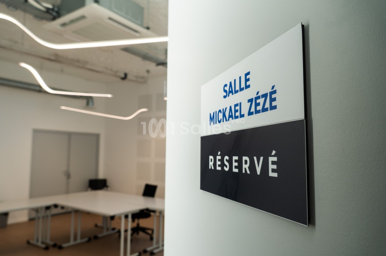 Panneau indiquant ’Salle Mickael Zézé - Réservé’ devant une salle de réunion moderne et vide.