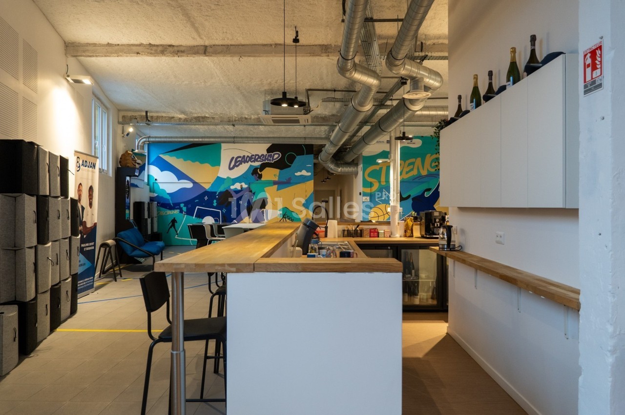 Espace de coworking moderne avec comptoir en bois, chaises hautes et fresque colorée sur le mur du fond.