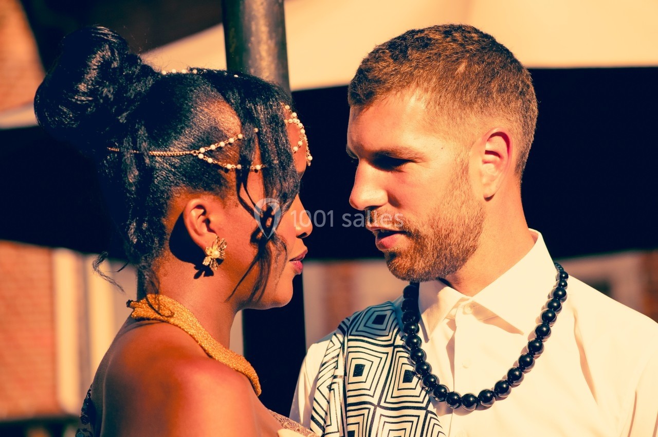 Un couple se regarde intensément sous une lumière chaude, en tenue élégante avec des accessoires distinctifs.