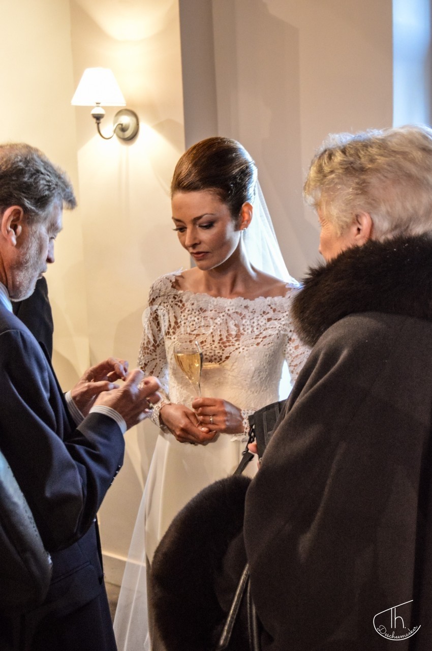 Une mariée en robe blanche discute avec deux invités dans un intérieur éclairé par une applique murale.