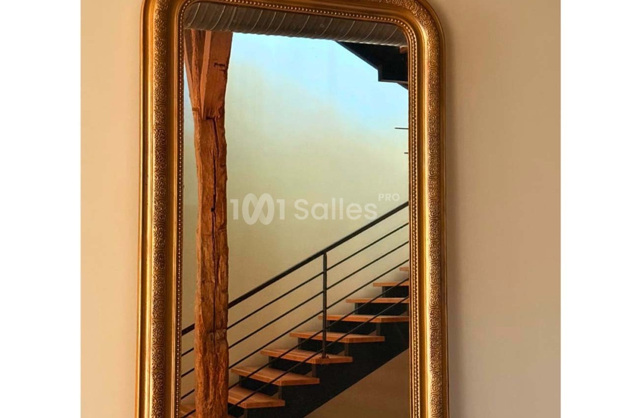 Miroir doré avec cadre orné, reflétant un escalier en bois et métal dans un intérieur lumineux.