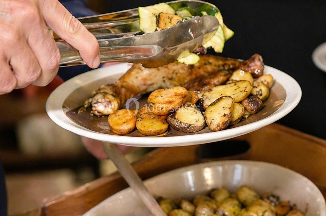Une assiette contenant un pilon de poulet rôti, des pommes de terre et des légumes servis avec des pinces.