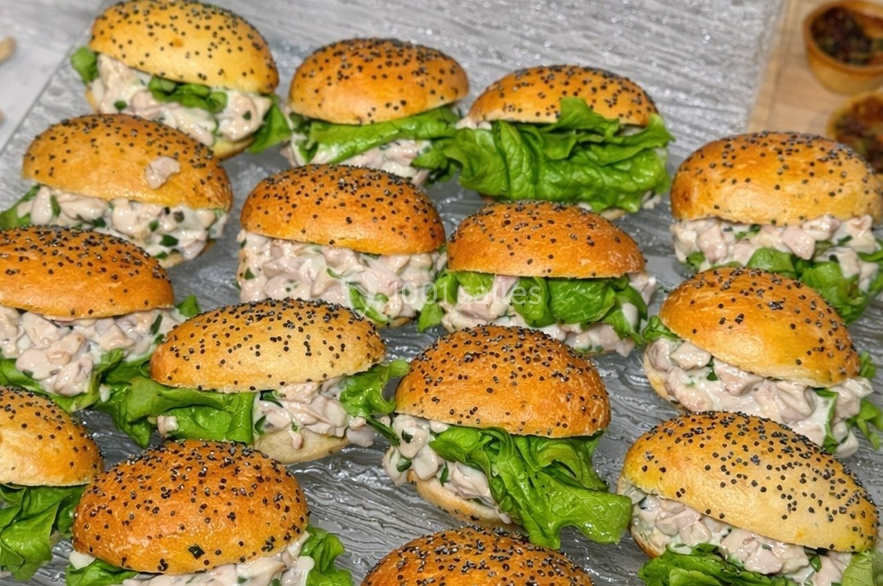 Petits pains garnis de salade verte et d'une préparation crémeuse, disposés sur un plateau transparent.