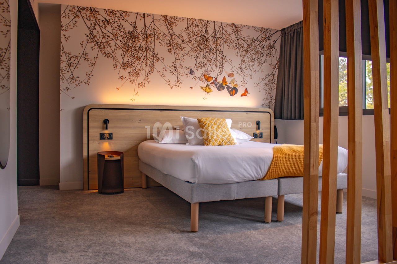 Chambre moderne avec un lit double, décorée de motifs floraux muraux et éclairée par une lumière douce.