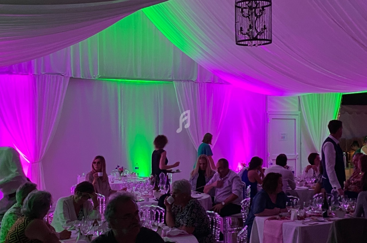 Salle de réception éclairée de lumières violettes et vertes, avec des invités assis à des tables dressées.