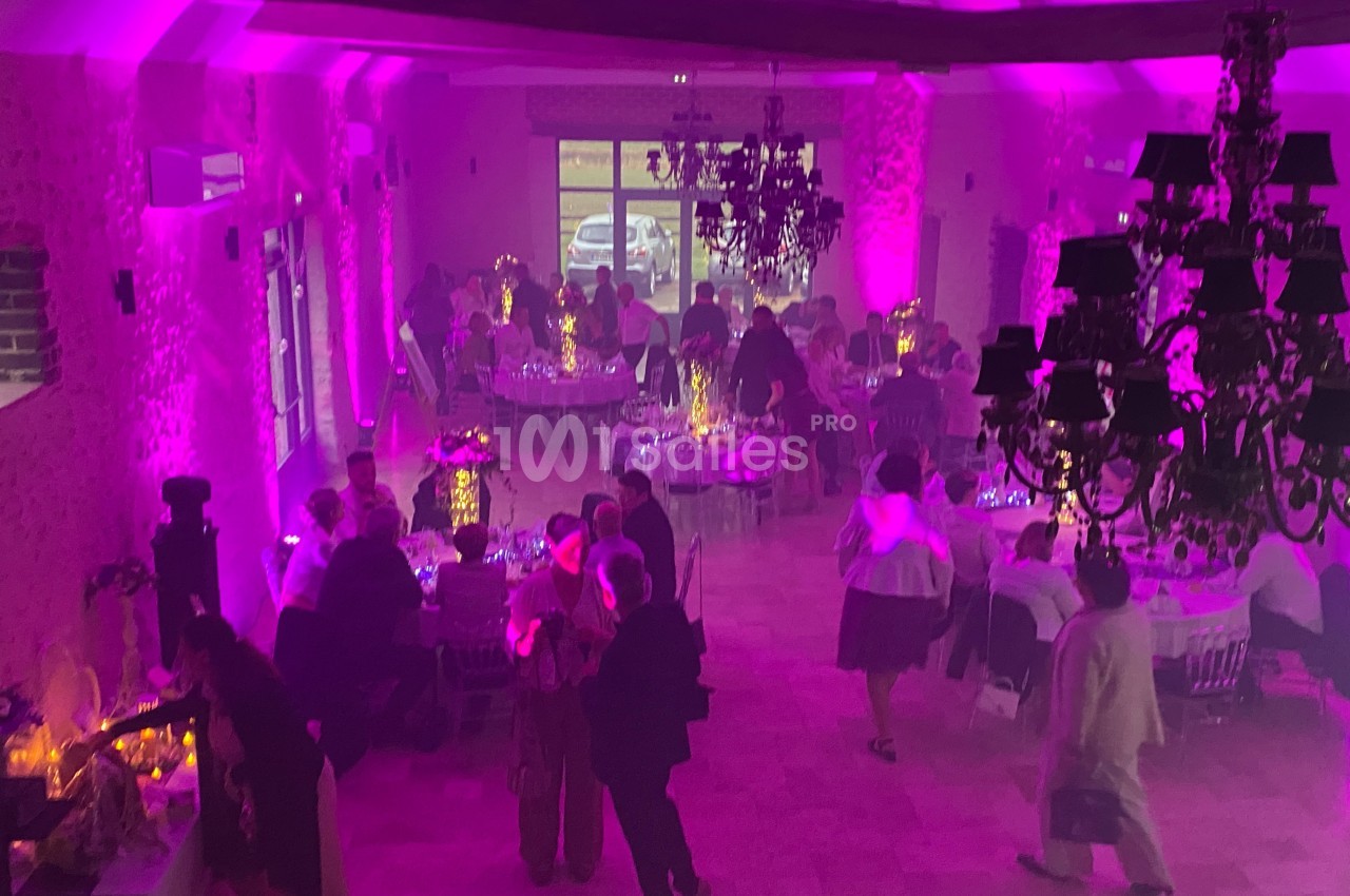 Salle de réception éclairée en rose avec des invités discutant et dînant autour de tables décorées.