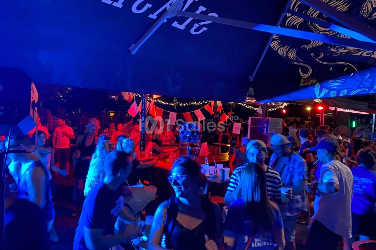Groupe de personnes dansant et socialisant sous des lumières colorées dans un espace extérieur festif.