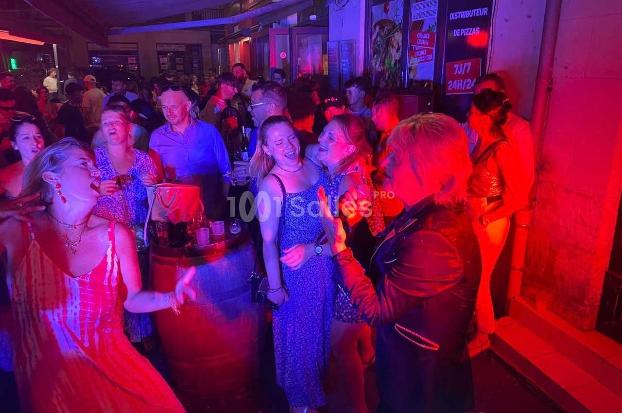 Groupe de personnes dans un bar animé, éclairé par des lumières rouges, certaines chantant et dansant.