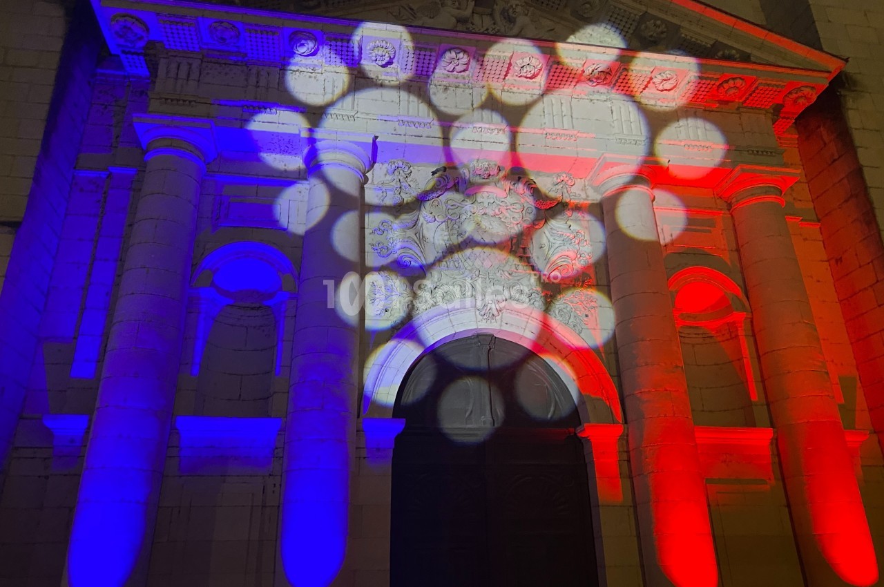 Façade d'un bâtiment éclairée par des projecteurs diffusant les couleurs bleu, blanc et rouge.