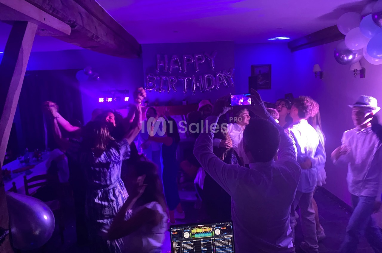 Personnes dansant et célébrant un anniversaire dans une salle décorée avec des lumières colorées et des ballons.