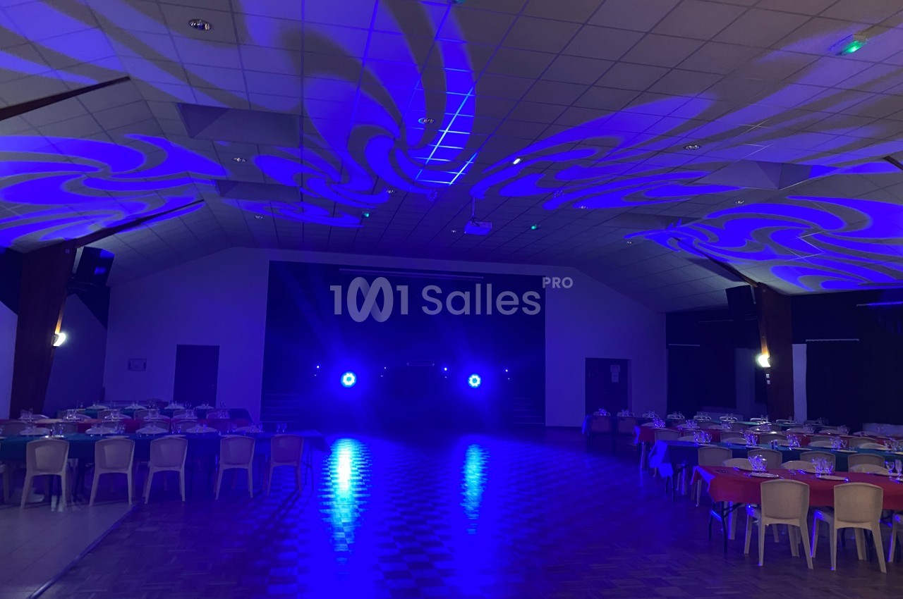 Salle de réception avec tables dressées et éclairage bleu projeté au plafond et sur le sol.