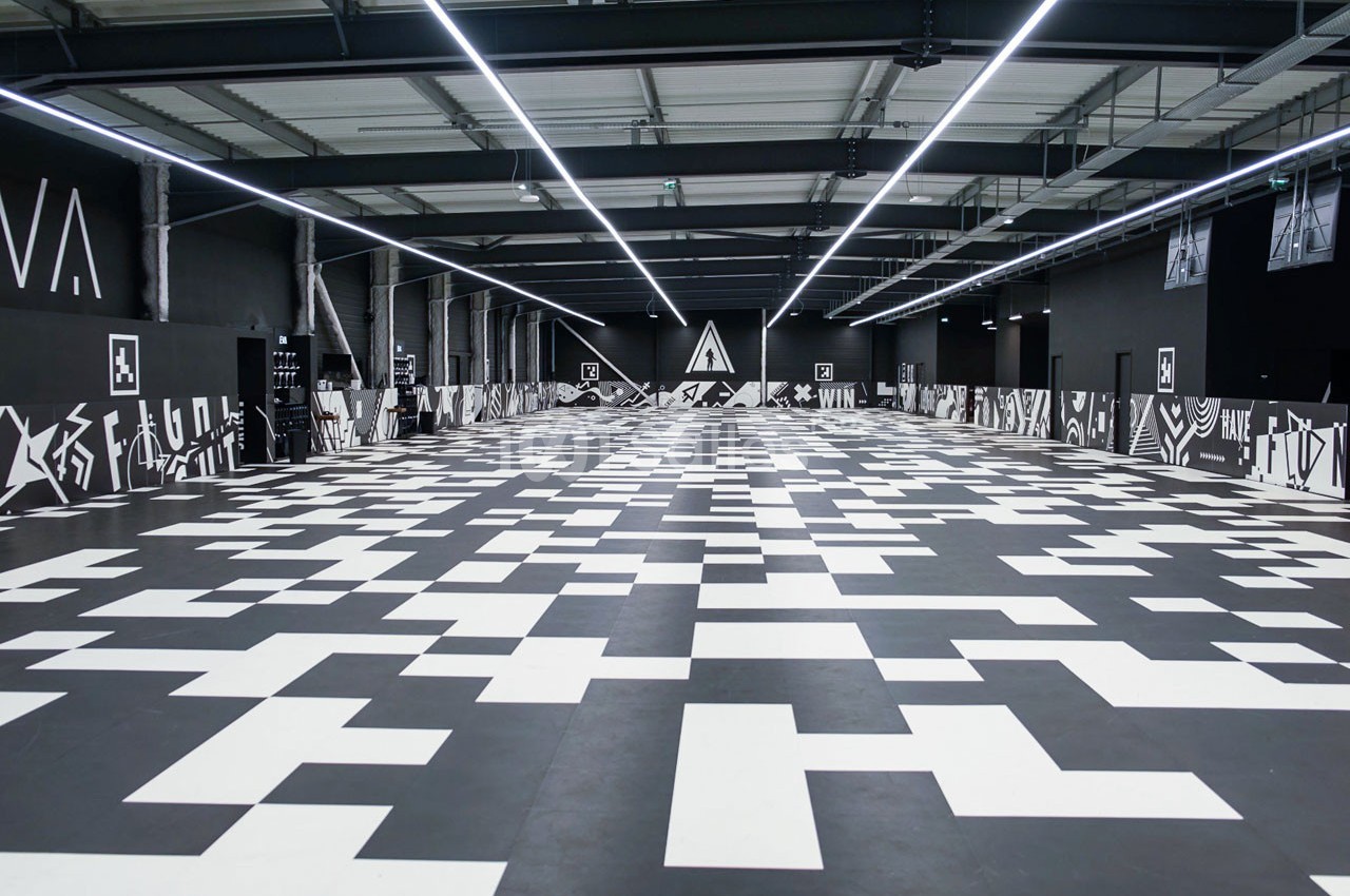 Salle intérieure spacieuse avec un sol noir et blanc à motifs géométriques et des murs décorés de graphismes abstraits.