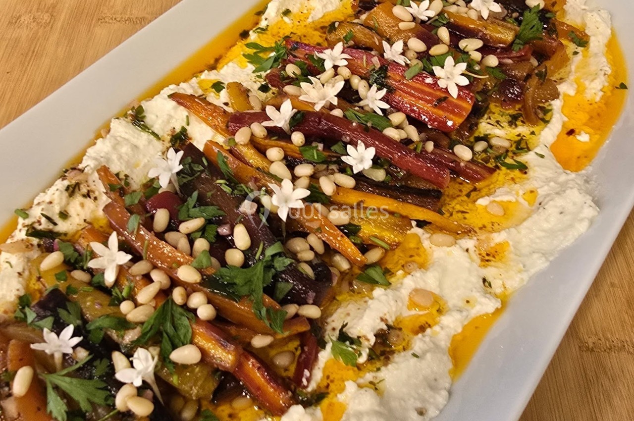 Plat de légumes rôtis colorés sur un lit de crème, garni de pignons de pin, herbes fraîches et fleurs comestibles.