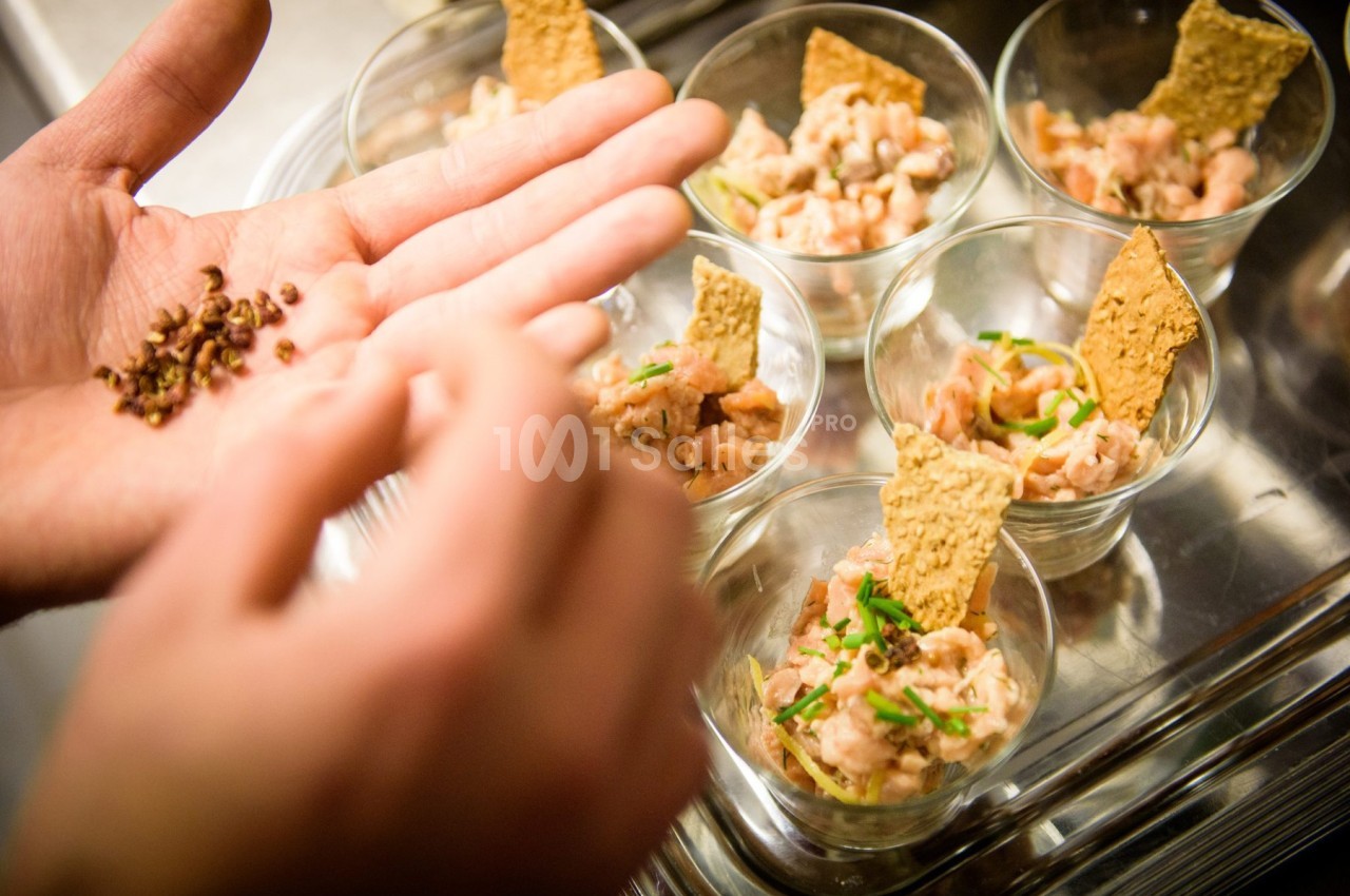 Préparation de verrines de tartare de saumon avec des crackers, une main ajoutant des épices en finition.