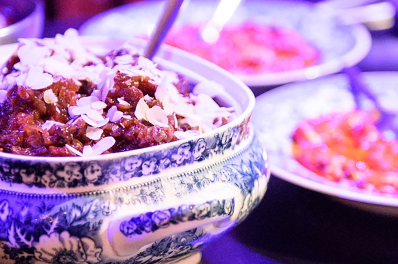 Plat en céramique décorée contenant un mets garni d'amandes effilées, entouré d'autres assiettes colorées.