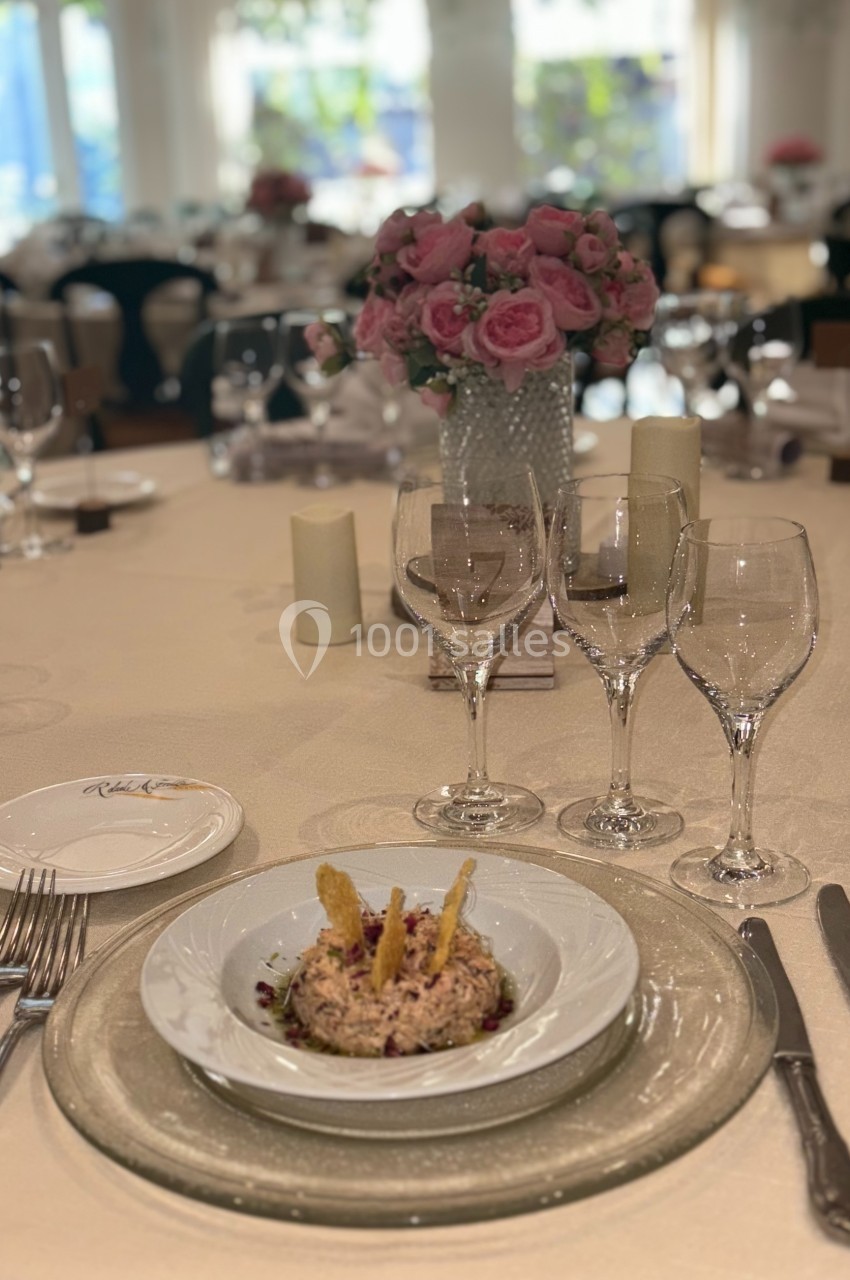 Table élégamment dressée avec une entrée servie dans une assiette, entourée de verres à vin et d'une décoration florale.