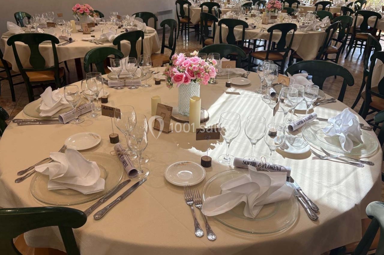 Salle de réception avec tables rondes dressées, nappes blanches, vaisselle élégante et centre de table floral.