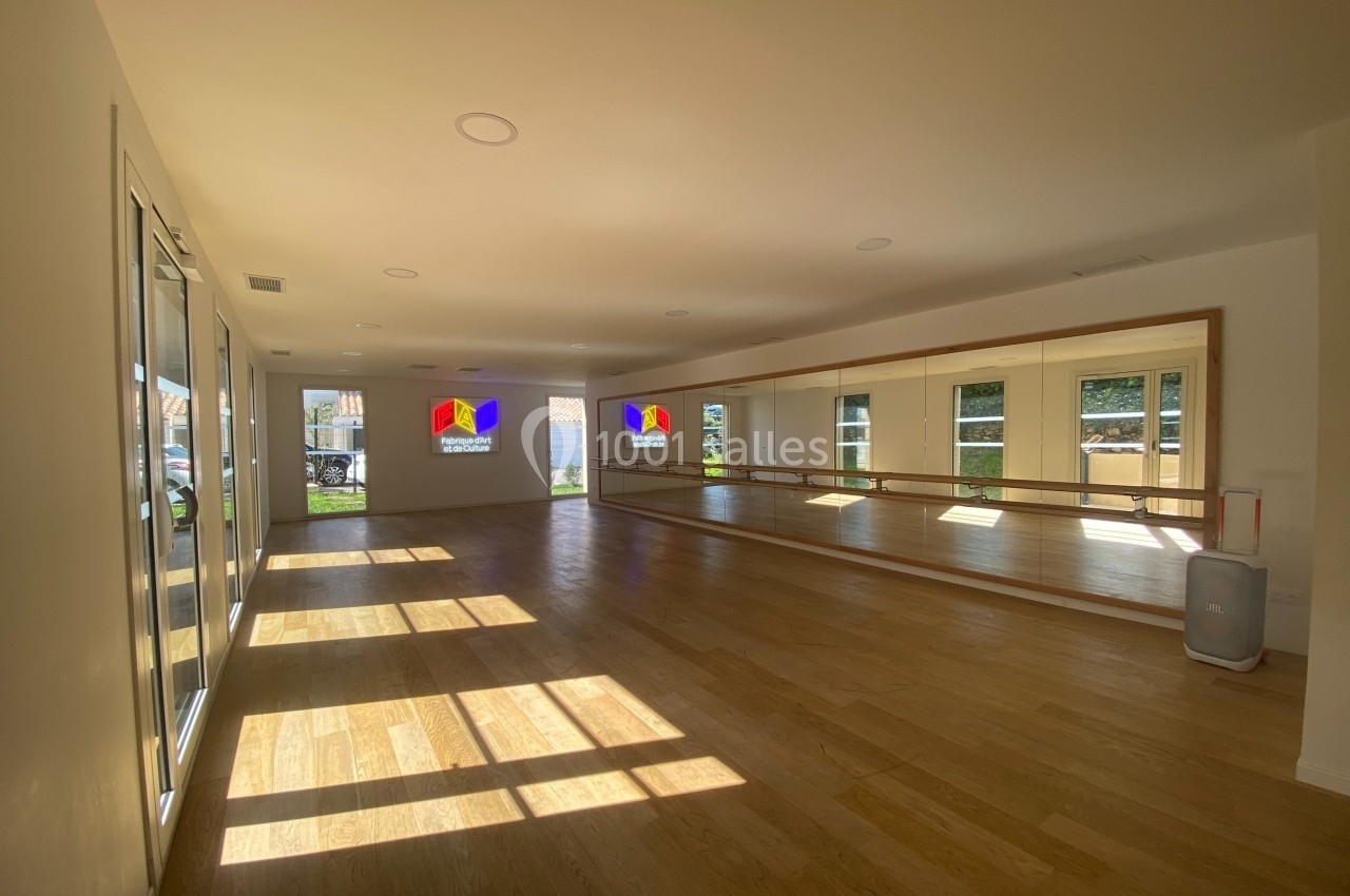 Salle lumineuse avec parquet, miroirs sur un mur et grandes fenêtres laissant entrer la lumière naturelle.