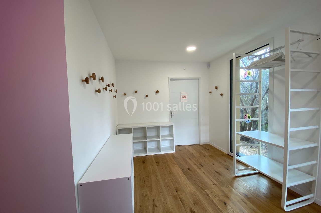 Pièce lumineuse avec parquet, étagères blanches, patères murales en bois et porte donnant sur l'extérieur.